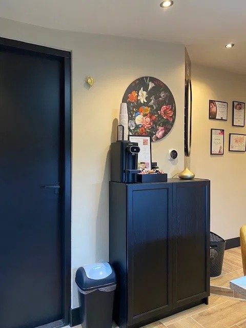 Een hoek van de studio met certificaten aan de muur, een klok met bloemen en een koffiemachine