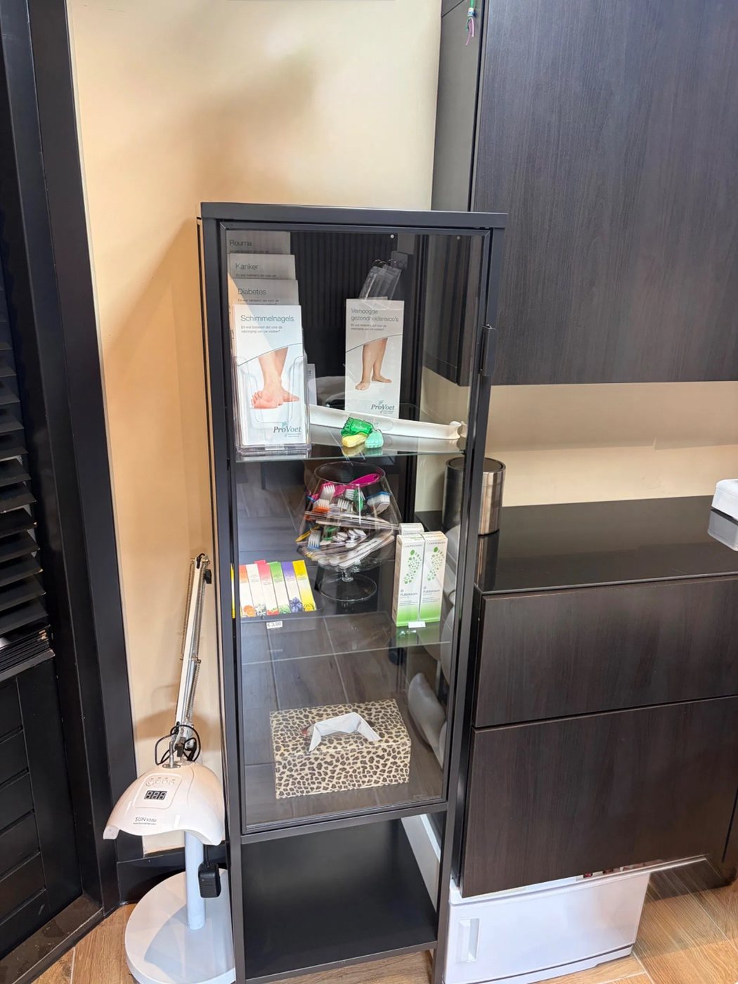 Een glazen vitrine met verzorgingsproducten en folders naast een nagellamp
